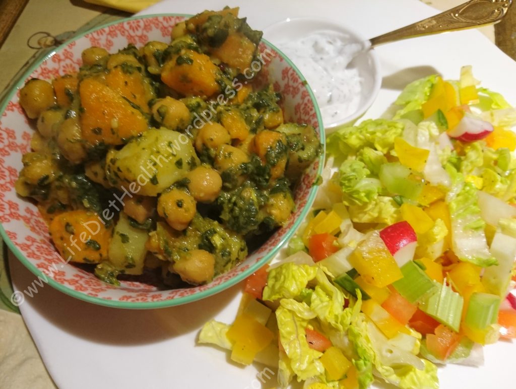 Dish or chickpea, potato and spinach curry with salad and raita sides
